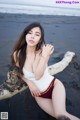 A woman in a white tank top and red panties sitting on a log on the beach.