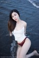 A woman in a white tank top and red bikini sitting in the water.