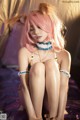 A woman with pink hair sitting on a bed.