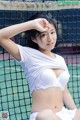 A woman in a white bikini sitting on a tennis court.