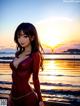 A woman in a red dress standing on a beach at sunset.