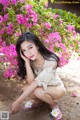 A woman sitting on the ground in front of a bush of flowers.