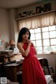 A woman in a red dress standing in front of a window.