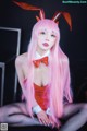 A woman with long pink hair wearing bunny ears and a bow tie.