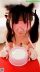 A little girl wearing a pink cat mask and holding a bowl of milk.