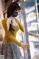 A woman wearing a face mask standing in front of a refrigerator.