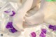 A woman's legs in white tights with purple petals on a bed.