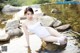 A woman in a white bathing suit sitting on a rock in the water.