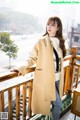 a woman standing on a balcony wearing a beige coat