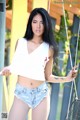 A woman in a white tank top and denim shorts posing on a swing.