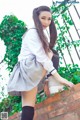 A woman in a school uniform leaning against a brick wall.