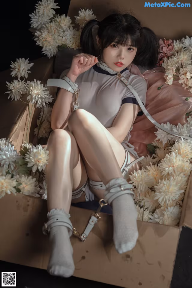 A woman sitting in a cardboard box surrounded by flowers.