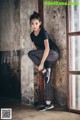 A woman in a black shirt and gray leggings leaning against a wall.