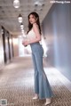 A woman in a white top and blue jeans standing in a hallway.