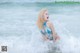 A woman in a blue bikini sitting in the ocean.