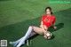 A woman in a red shirt and white socks sitting on a soccer field.