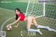 A woman in a red shirt and white socks is posing with a soccer ball.