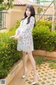 A woman in a white dress posing in front of yellow flowers.