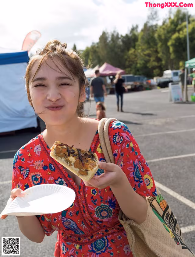 A young girl holding a plate of food in a parking lot.