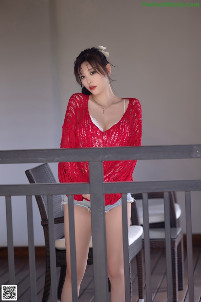 A woman in a red top and denim shorts posing on a balcony.