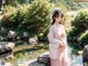 A woman in a pink kimono standing in front of a pond.