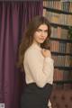 A woman in a white shirt and black skirt posing in front of a bookcase.