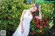 A woman in a white dress posing in front of a bush.