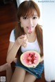 A woman eating a slice of watermelon with a spoon.