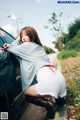 A woman leaning against the side of a car with her back to the camera.