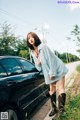 A woman standing next to a black car on the side of a road.