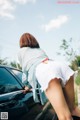 A woman leaning on the hood of a black car.