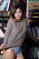 A woman in shorts and a sweater posing in front of a bookshelf.