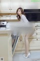 A woman in a white dress is standing in a kitchen.