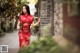 A woman in a red cheongsam leaning against a brick wall.