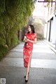 A woman in a red cheongsam standing on a sidewalk.