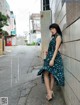 A woman leaning against a wall in a blue dress.