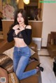 A woman in a black top and jeans posing on a couch.